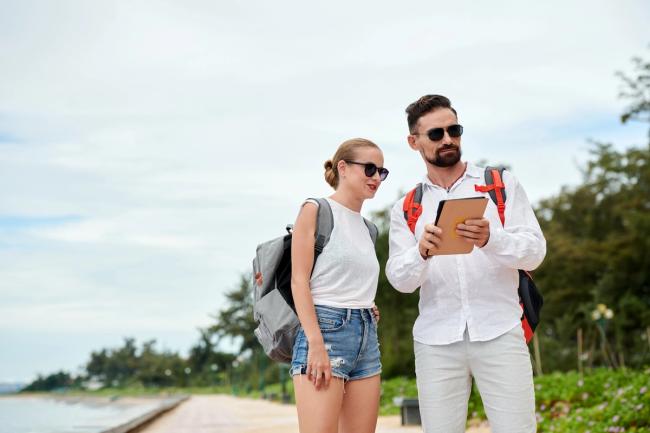 Two travelers using a tablet to help them with their trip while on a beach