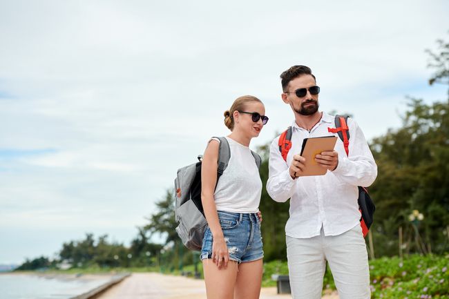 Two travelers using a tablet to help them with their trip while on a beach