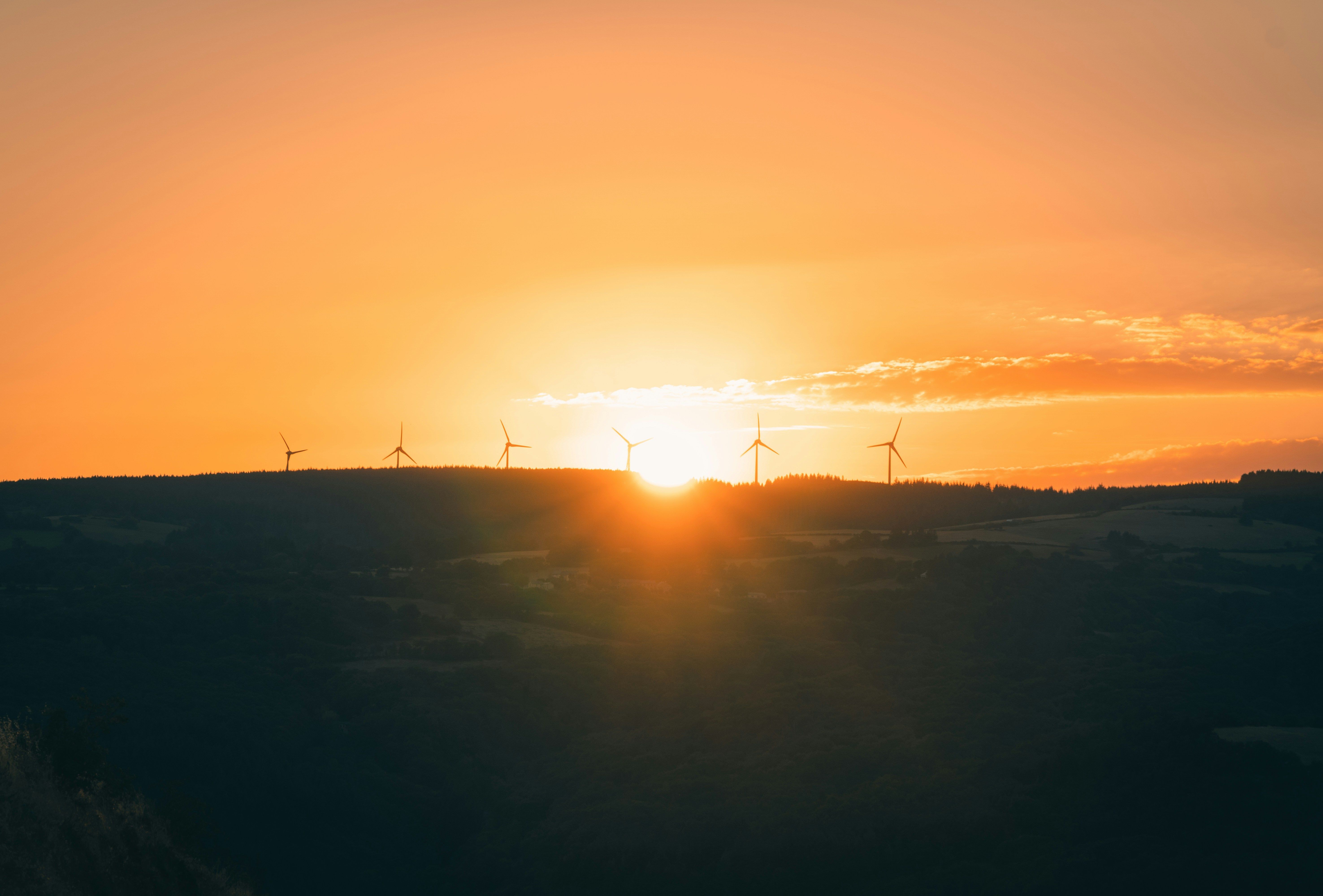 the sun is setting behind a row of wind turbines on a hill .