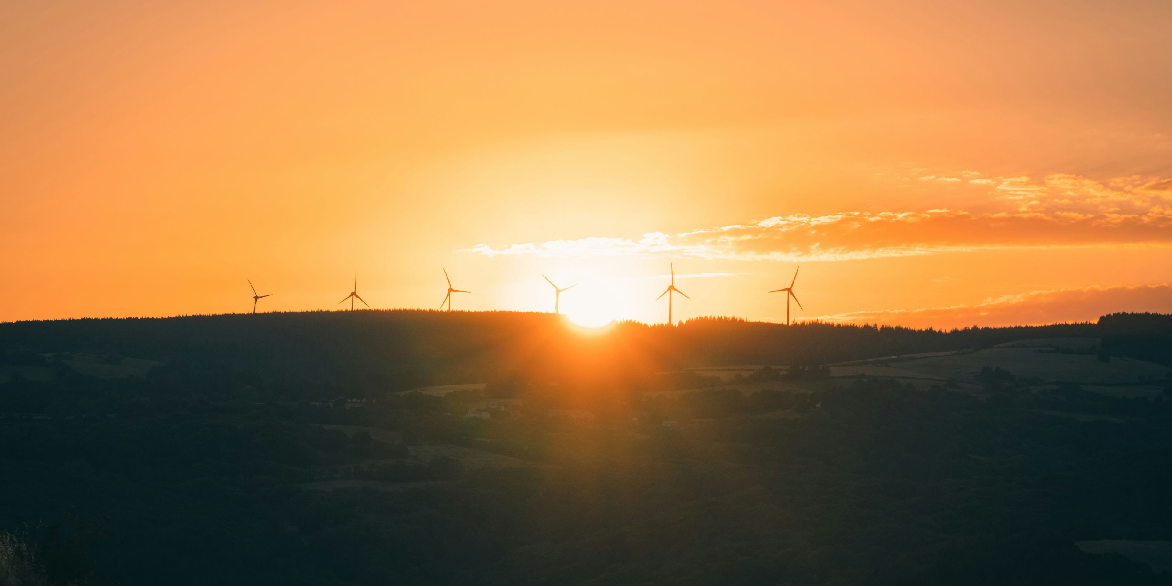 the sun is setting behind a row of wind turbines on a hill .