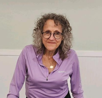 Portrait of a smiling community member wearing glasses and a purple top.