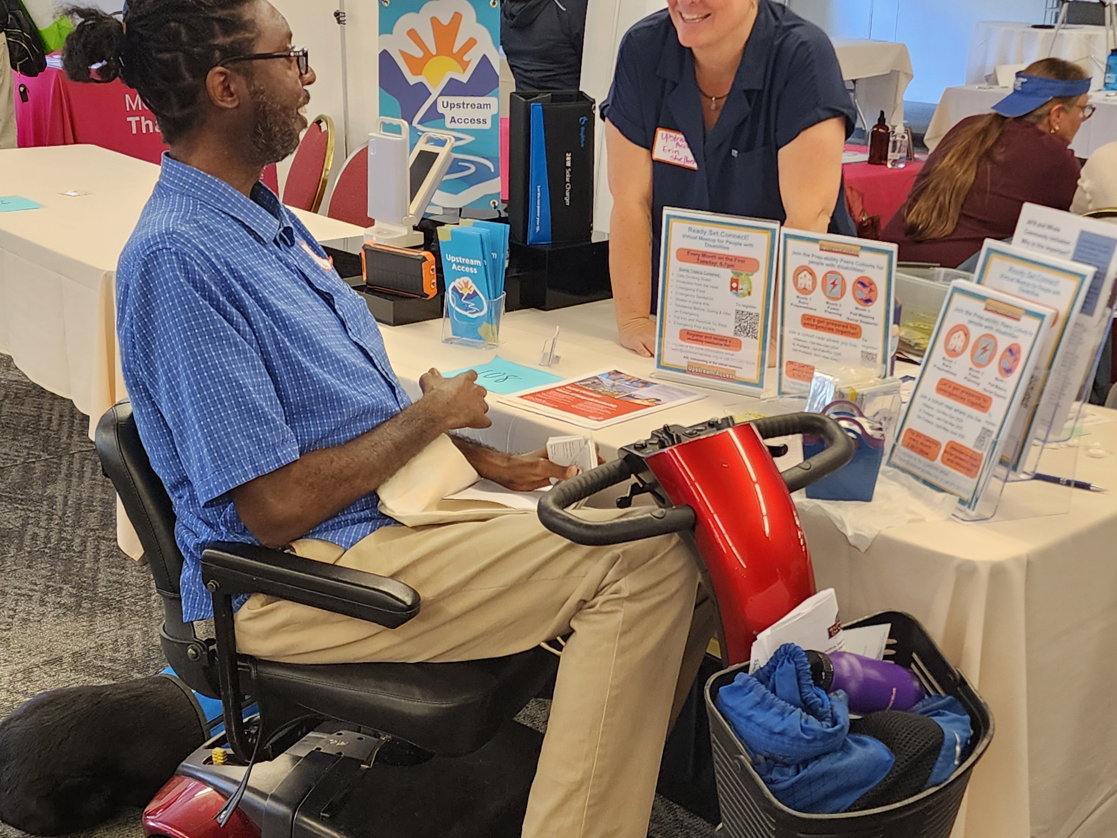 Person in a motorized chair interacting with an Upstream Access booth at a convention.