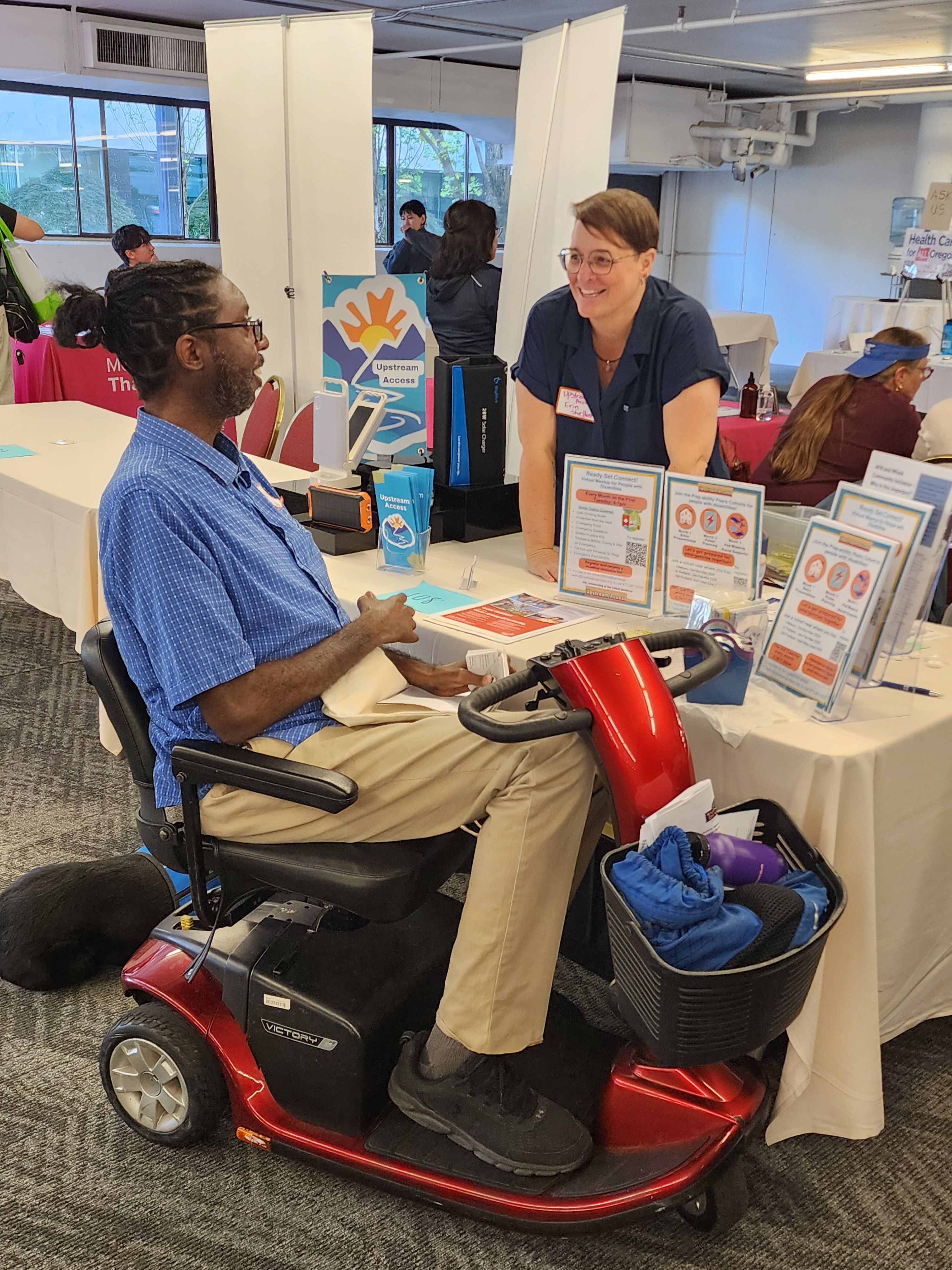 Person in a motorized chair interacting with an Upstream Access booth at a convention.