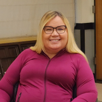 Portrait of a smiling community member wearing glasses and a pink jacket