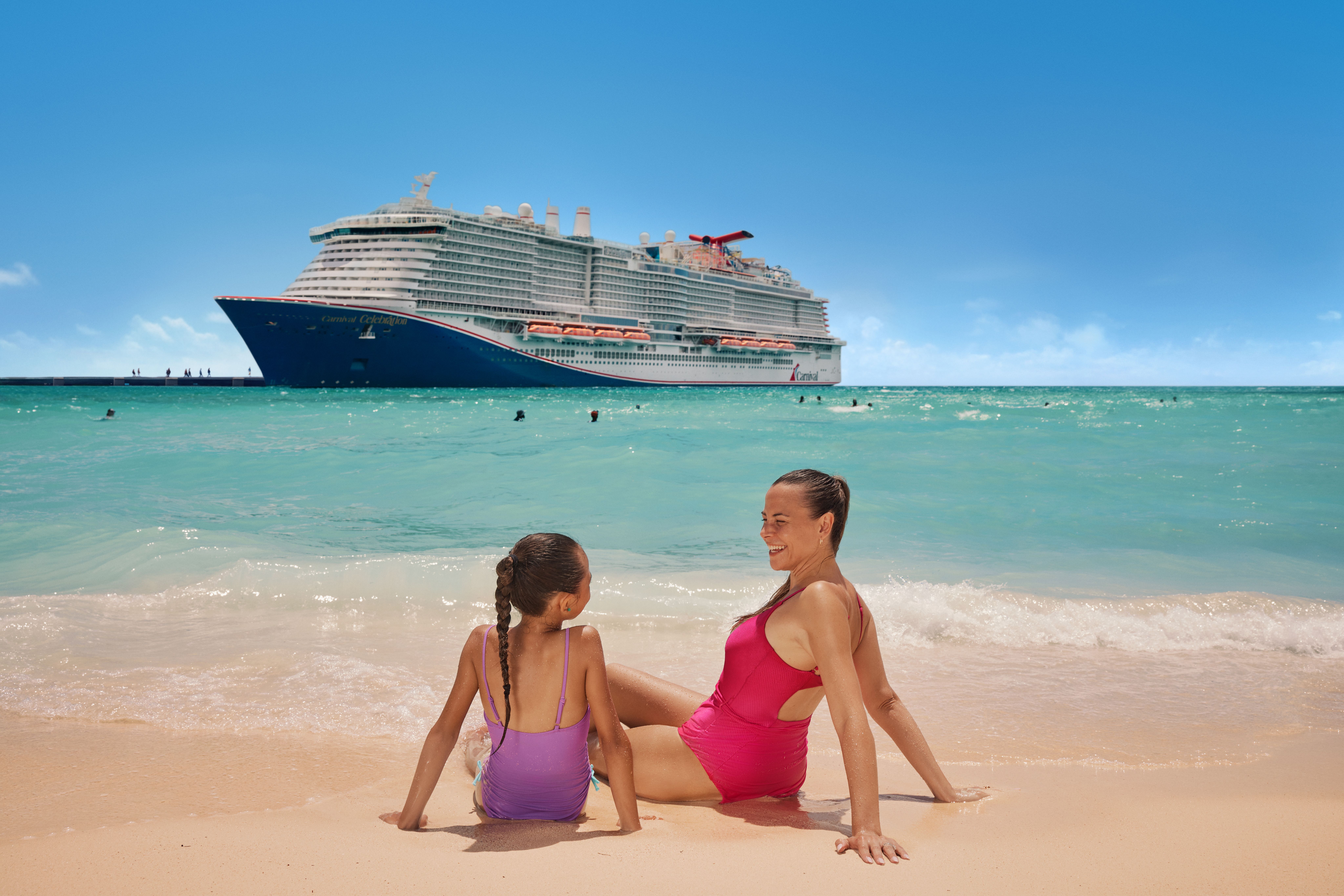 Mother and daughter lounging in the sand in front of Carnival cruise ship