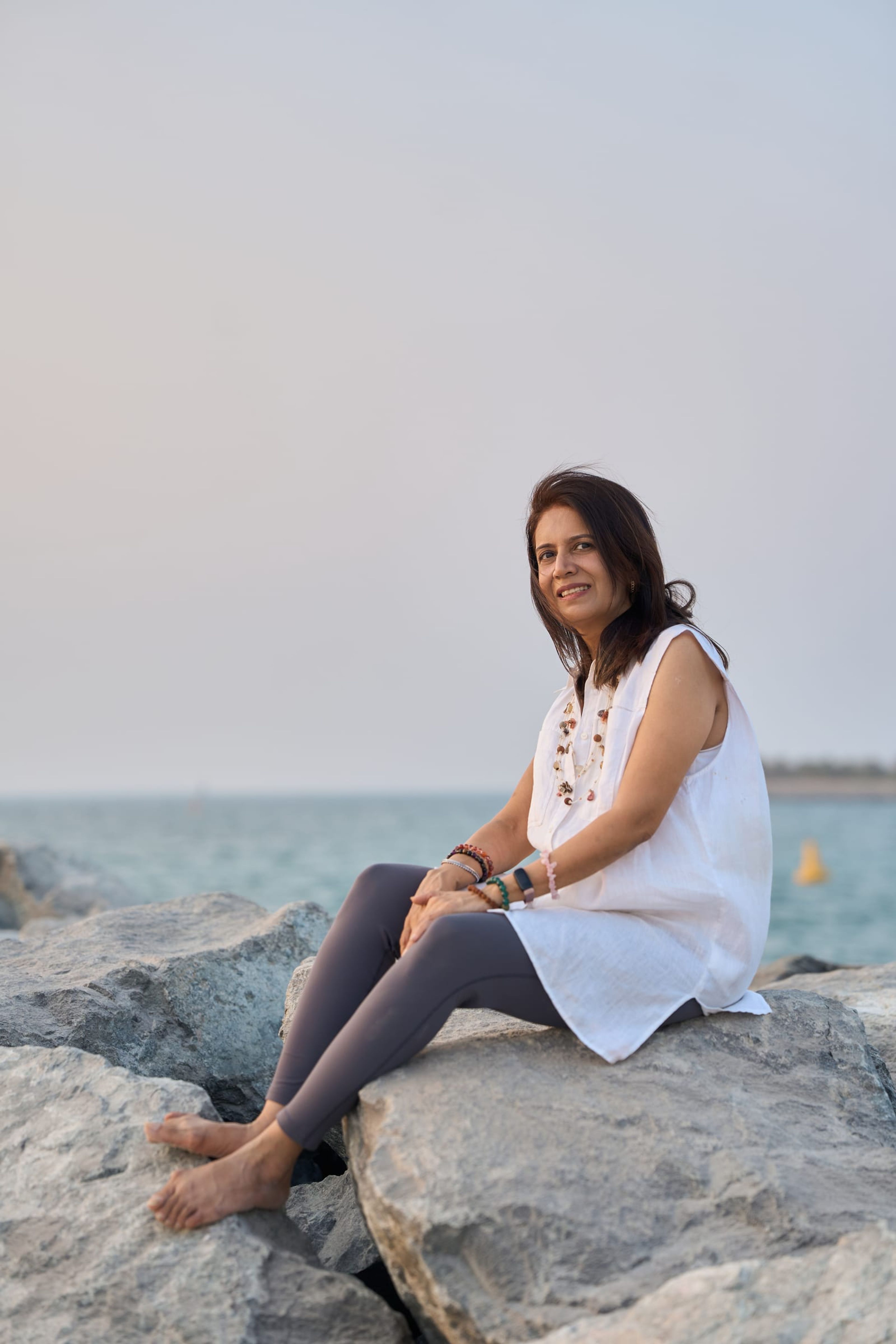 Manisha sitting on the rocks by the sea, smiling