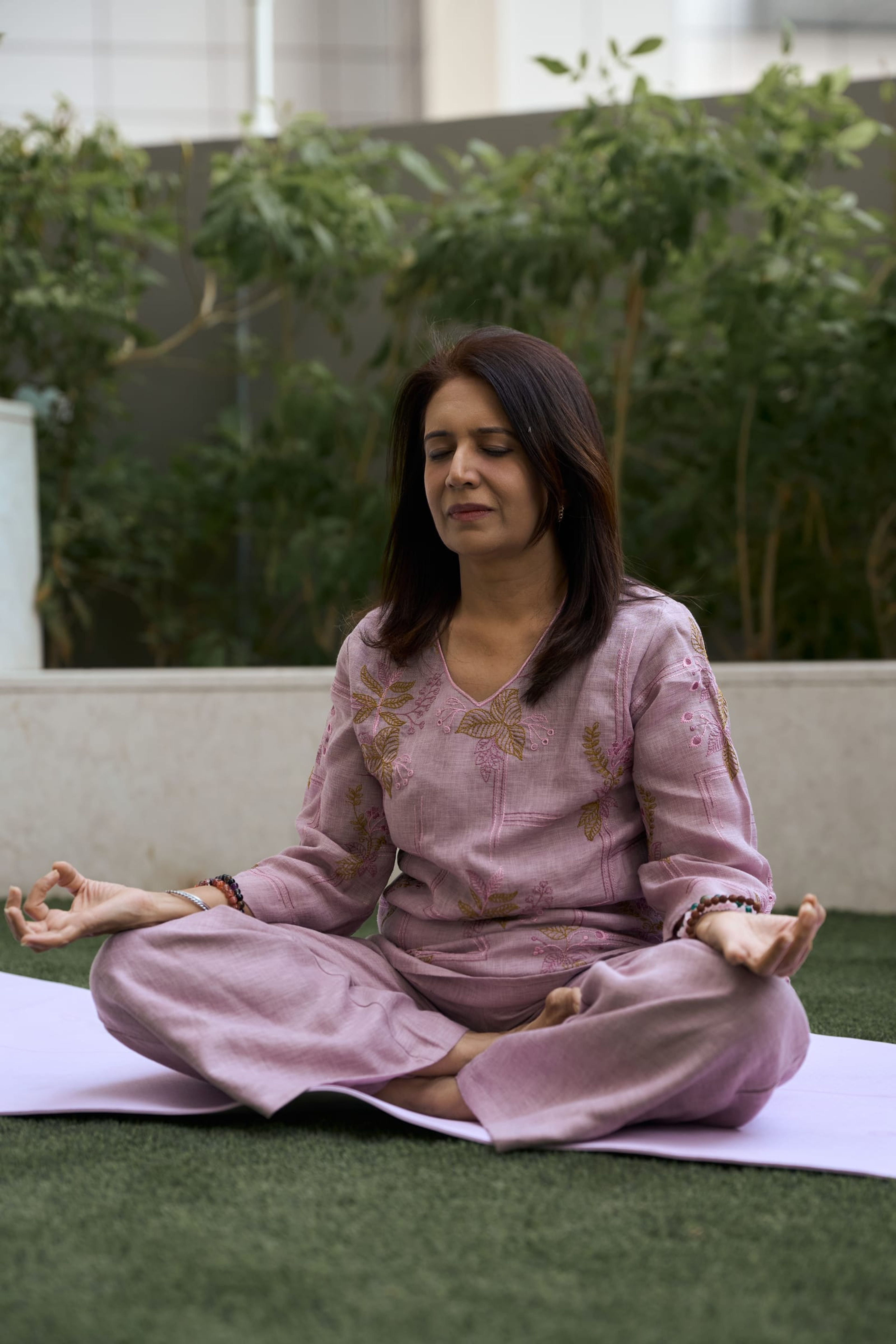Manisha meditating cross-legged outdoors among green plants