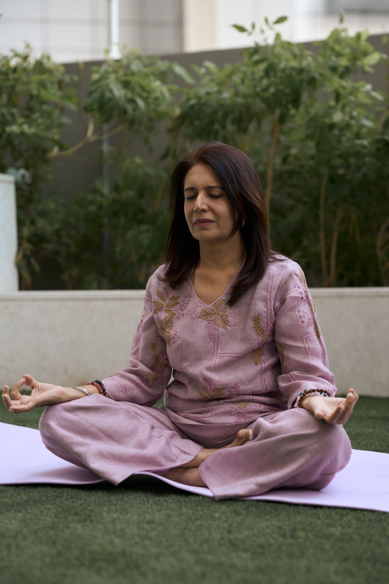 Manisha meditating cross-legged outdoors among green plants