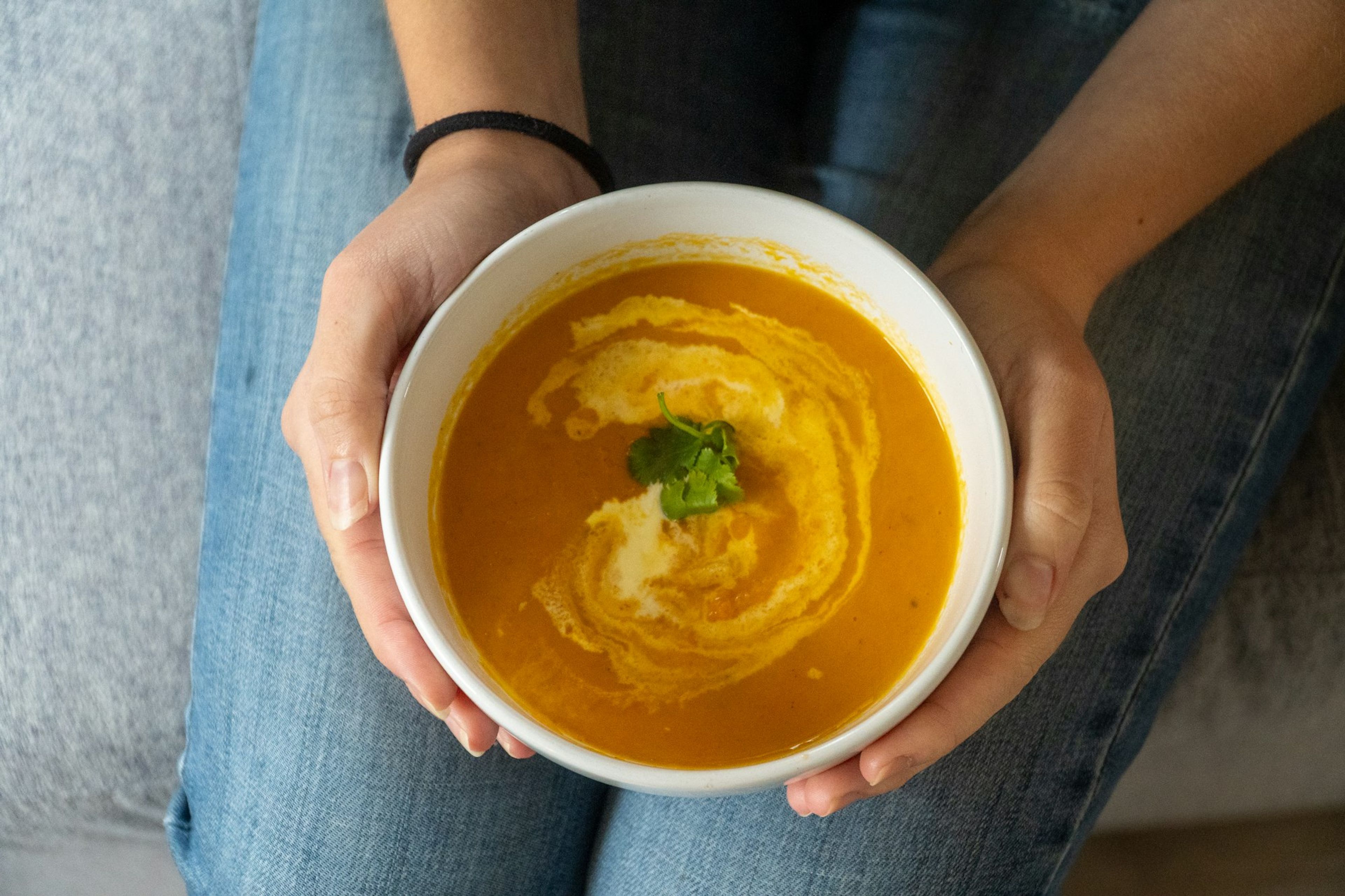 Hands holding a bowl of creamy orange soup