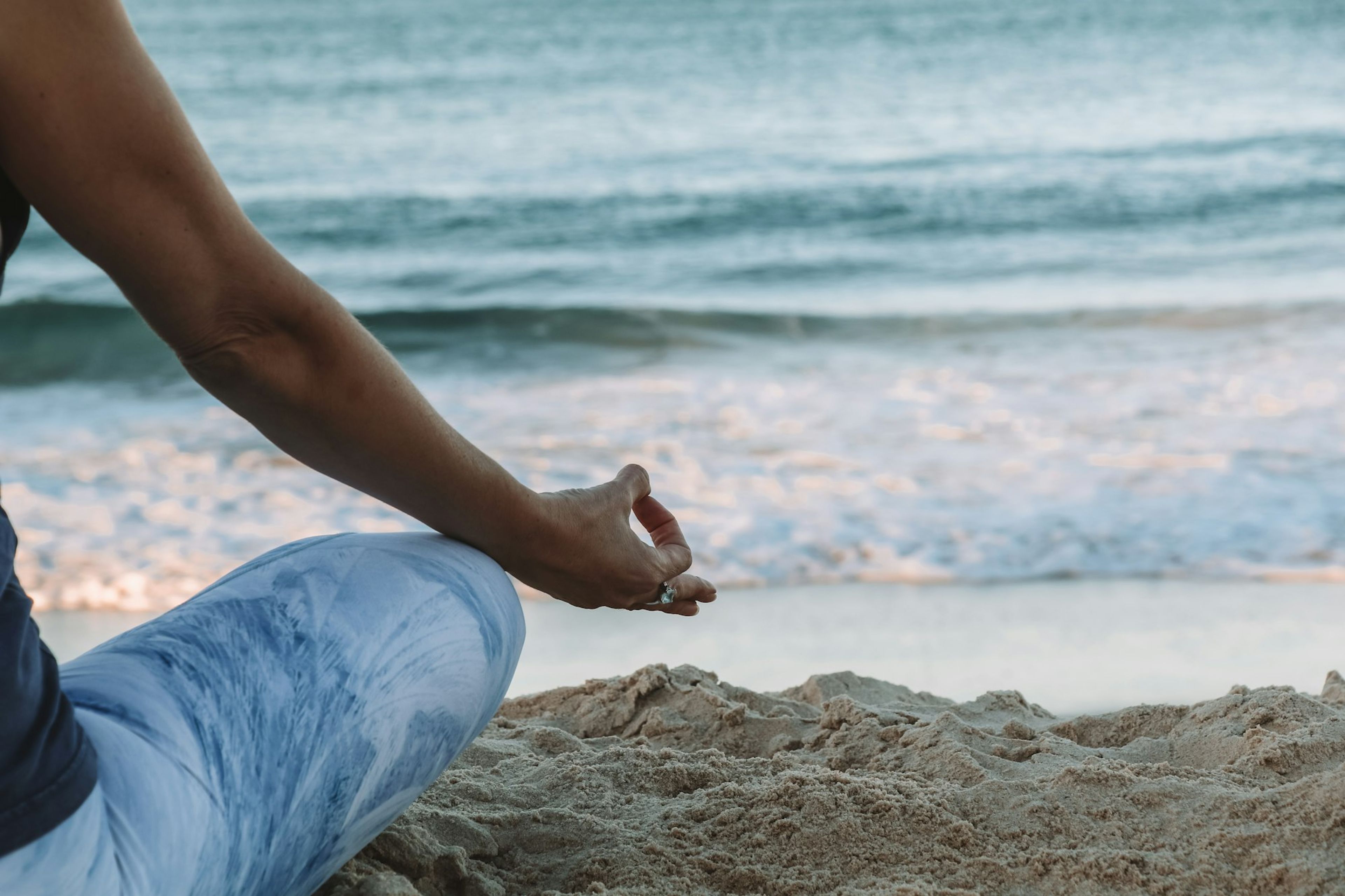 Hand resting in a mudra on a sandy beach