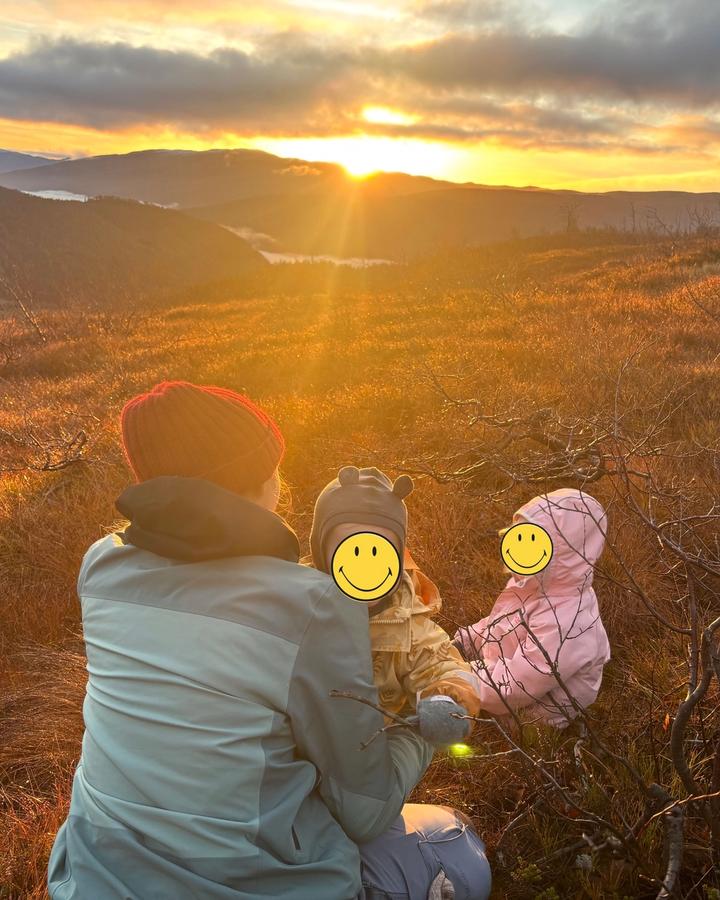 En voksen og to barn sitter i lyngen og ser på soloppgangen over åsene.