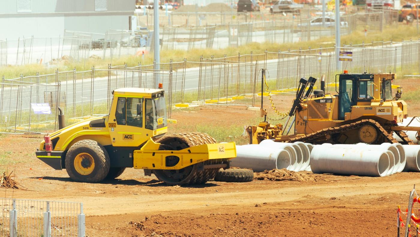Alt Text: Yellow soil compactor roller and CAT D6T bulldozer parked next to concrete drainage pipes on an active industrial construction site in Australia.