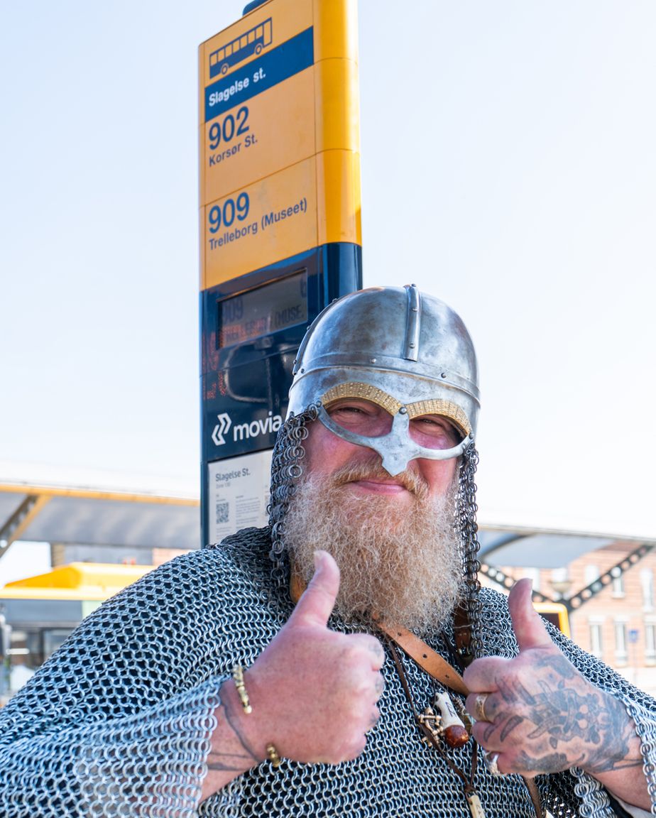 Mand i ringbrynje og vikingehjelm giver thumbs up ved busstoppestedet til Trelleborg Museet.