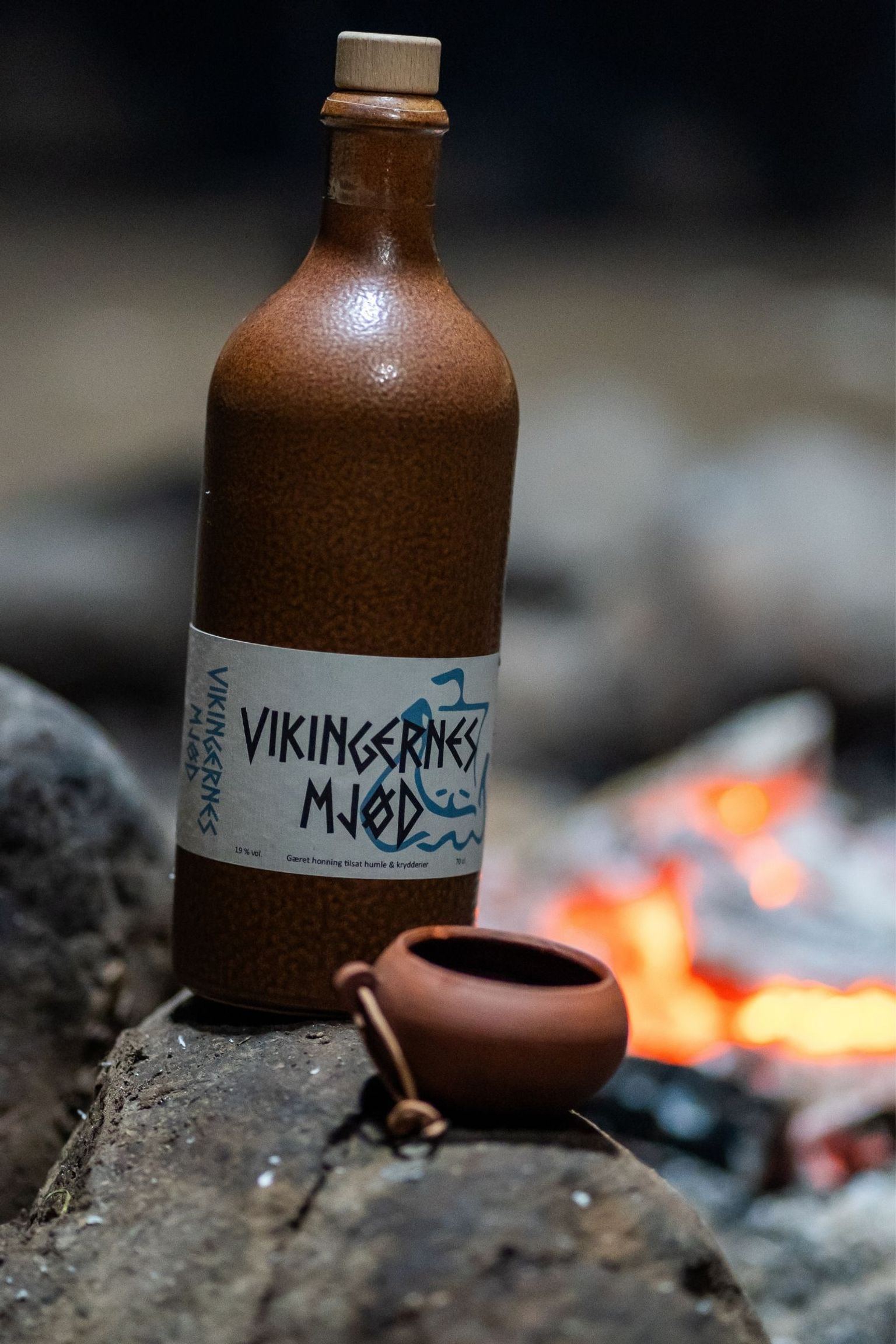 Mjød og kop i fokus ved siden af et bål