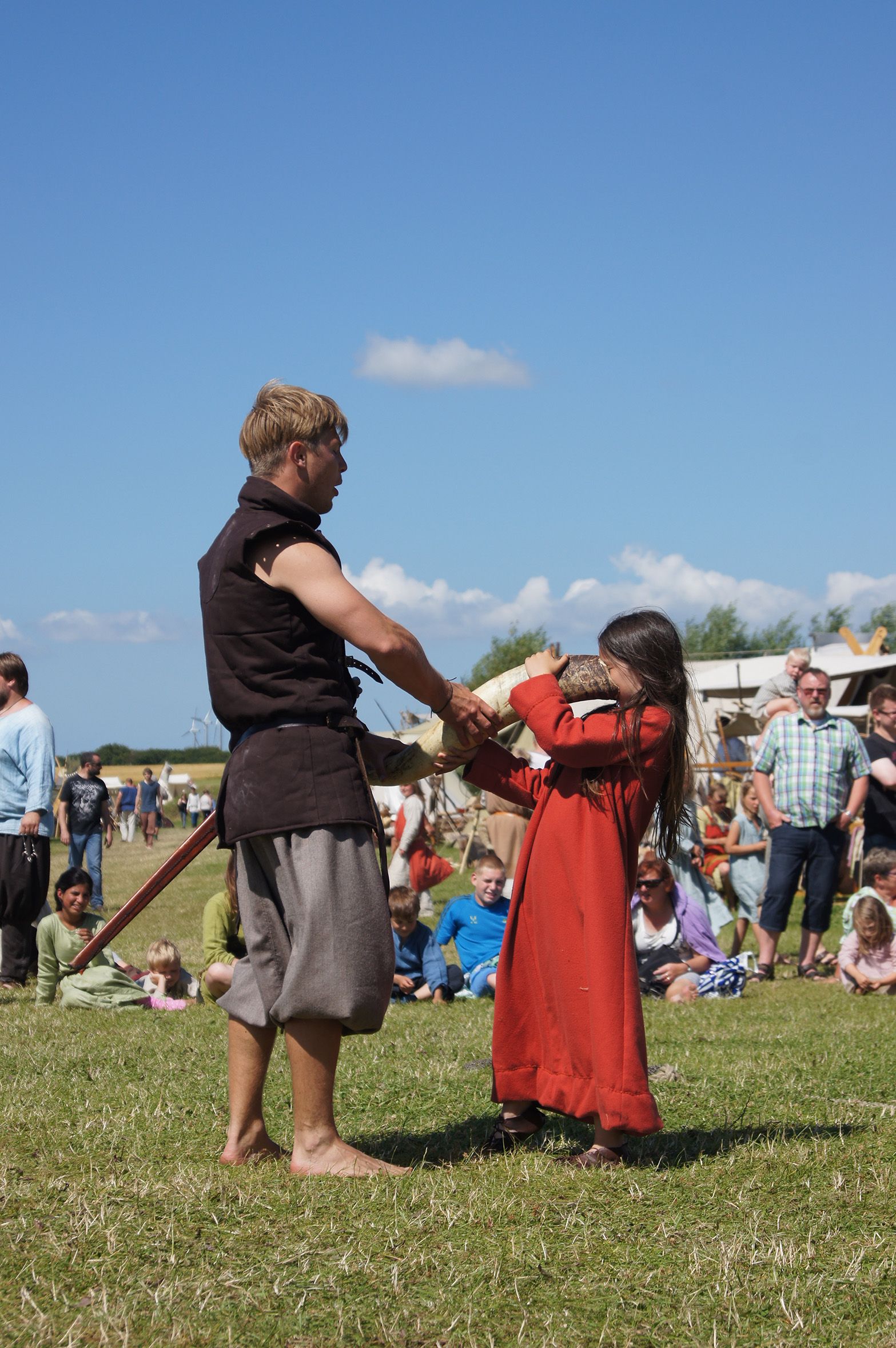 Pige i historisk kostume drikker af drikkehorn under levende rollespil med tilskuere i baggrunden