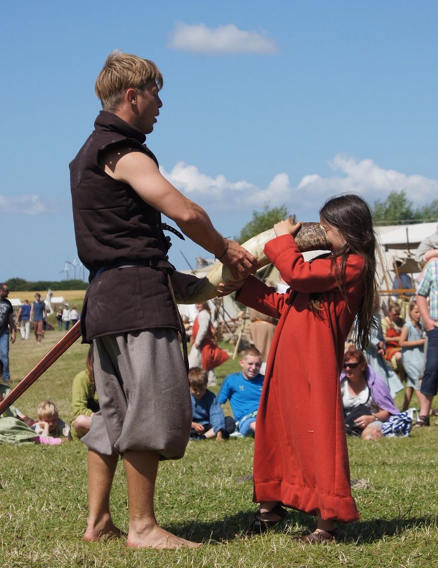 Pige i historisk kostume drikker af drikkehorn under levende rollespil med tilskuere i baggrunden
