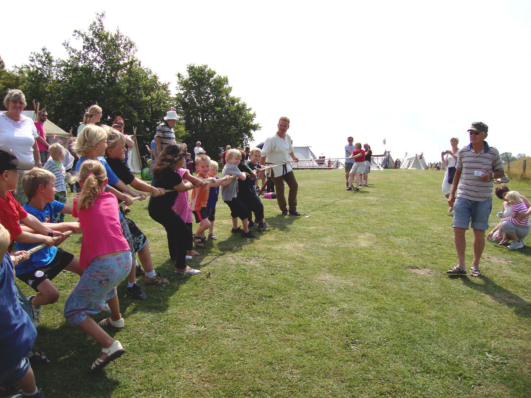 Børn og voksne i gang med tovtrækning på Trelleborgs grønne arealer en sommerdag.