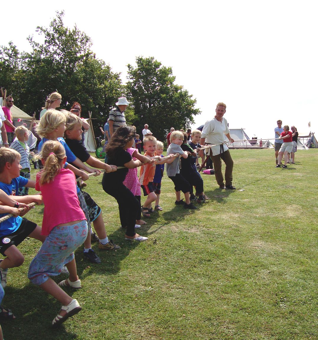 Børn og voksne i gang med tovtrækning på Trelleborgs grønne arealer en sommerdag.
