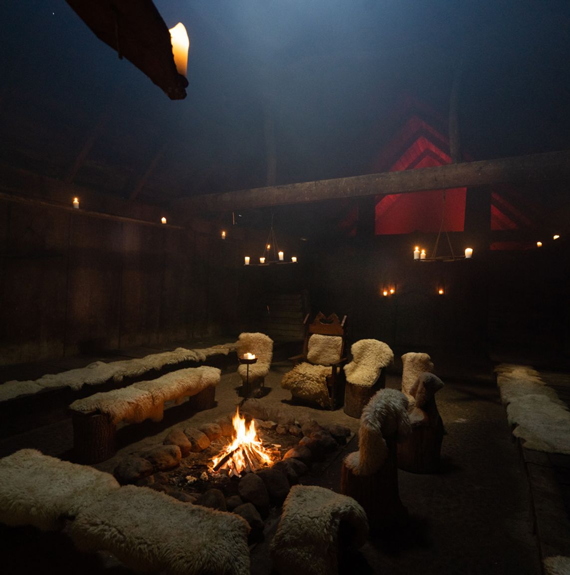 Et bål knitrer indenfor i langhuset med bænke rundt omkring