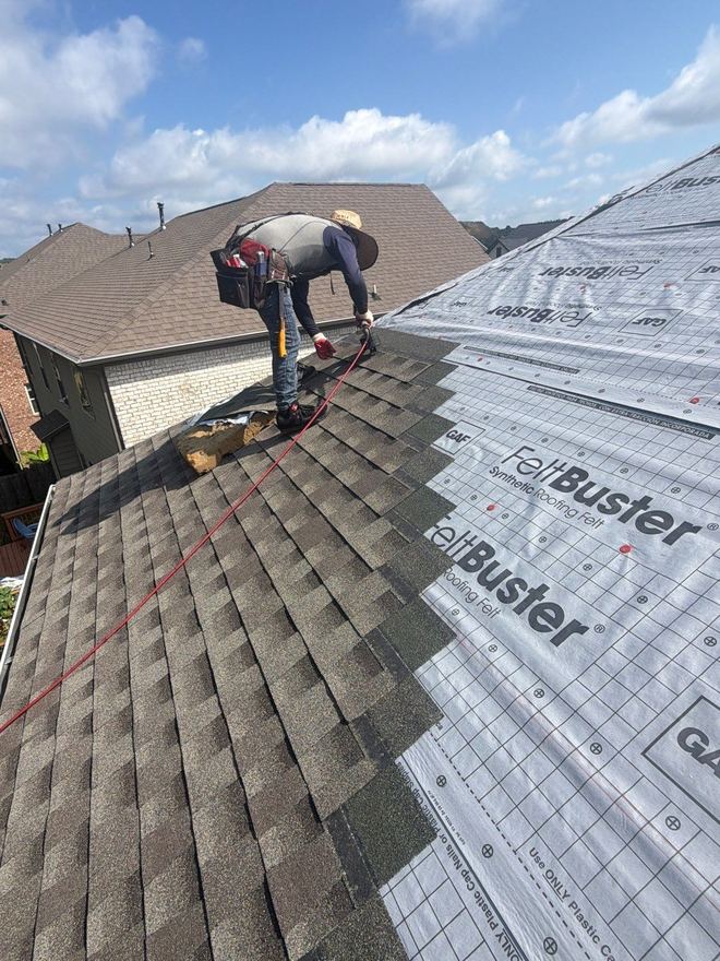 Roofer nailing shingles over synthetic underlayment part-way across a hip roof
