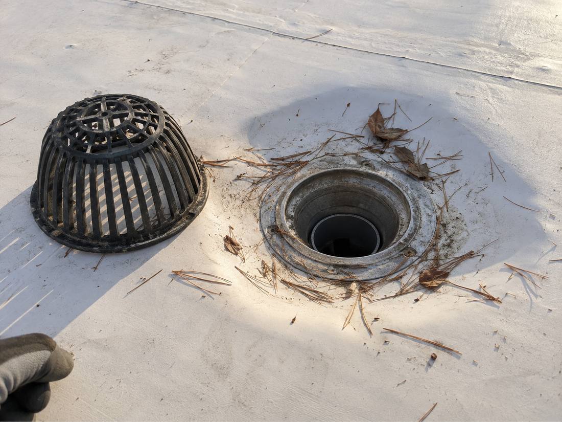 Flat roof drain with the strainer lifted aside and leaf debris cleared from the sump