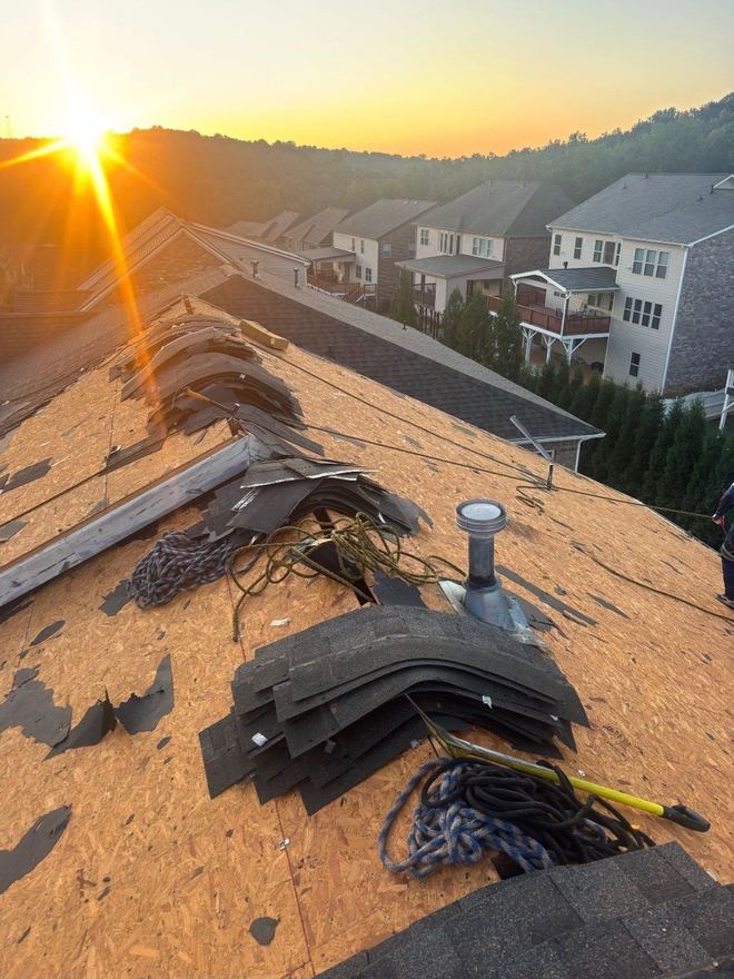 Tear-off in progress at sunrise, with bundles of new shingles staged on the deck