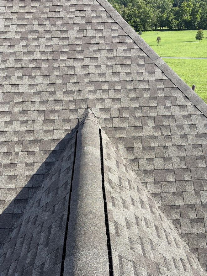 New ridge cap and shingles above an open green field