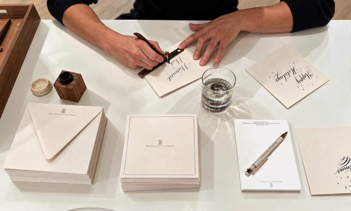 Close view of hands writing a card with a dip pen beside envelopes