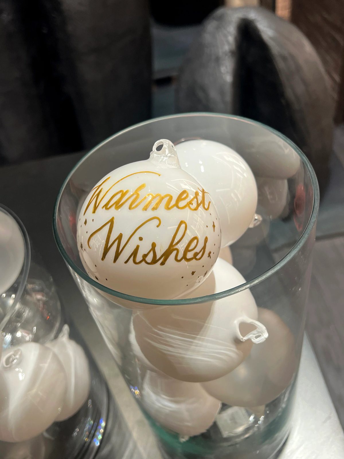 White ornament with gold Warmest Wishes lettering in a glass bowl