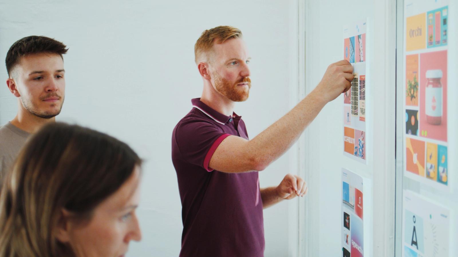Drei Personen stehen im Corporate Design Workshop vor mehreren Plakaten