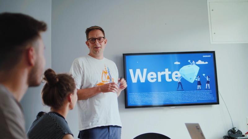 Ein Mann präsentiert vor einer Gruppe eine Folie zum Thema „Werte“ auf einem großen Bildschirm.