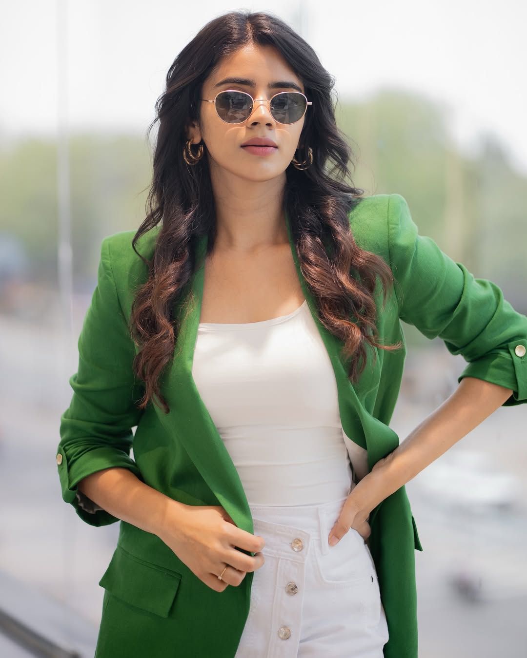 Creator Soundariya Nanjundan wearing a stylish green blazer with sunglasses, posing confidently in a modern outdoor setting
