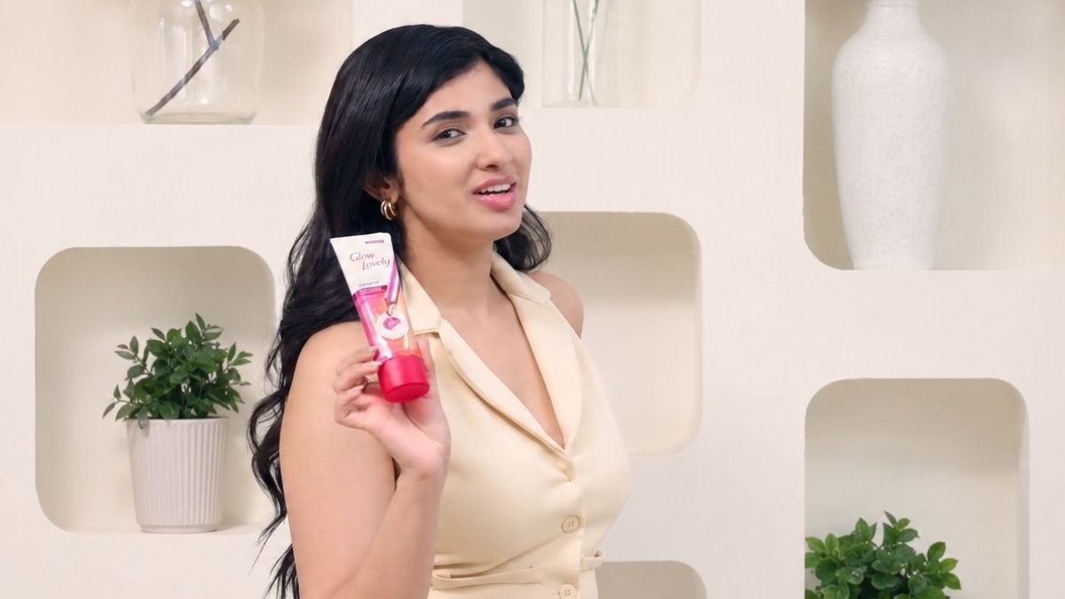Creator Pragya Nagra holding a skincare product in a bright indoor studio setting, wearing a beige sleeveless outfit