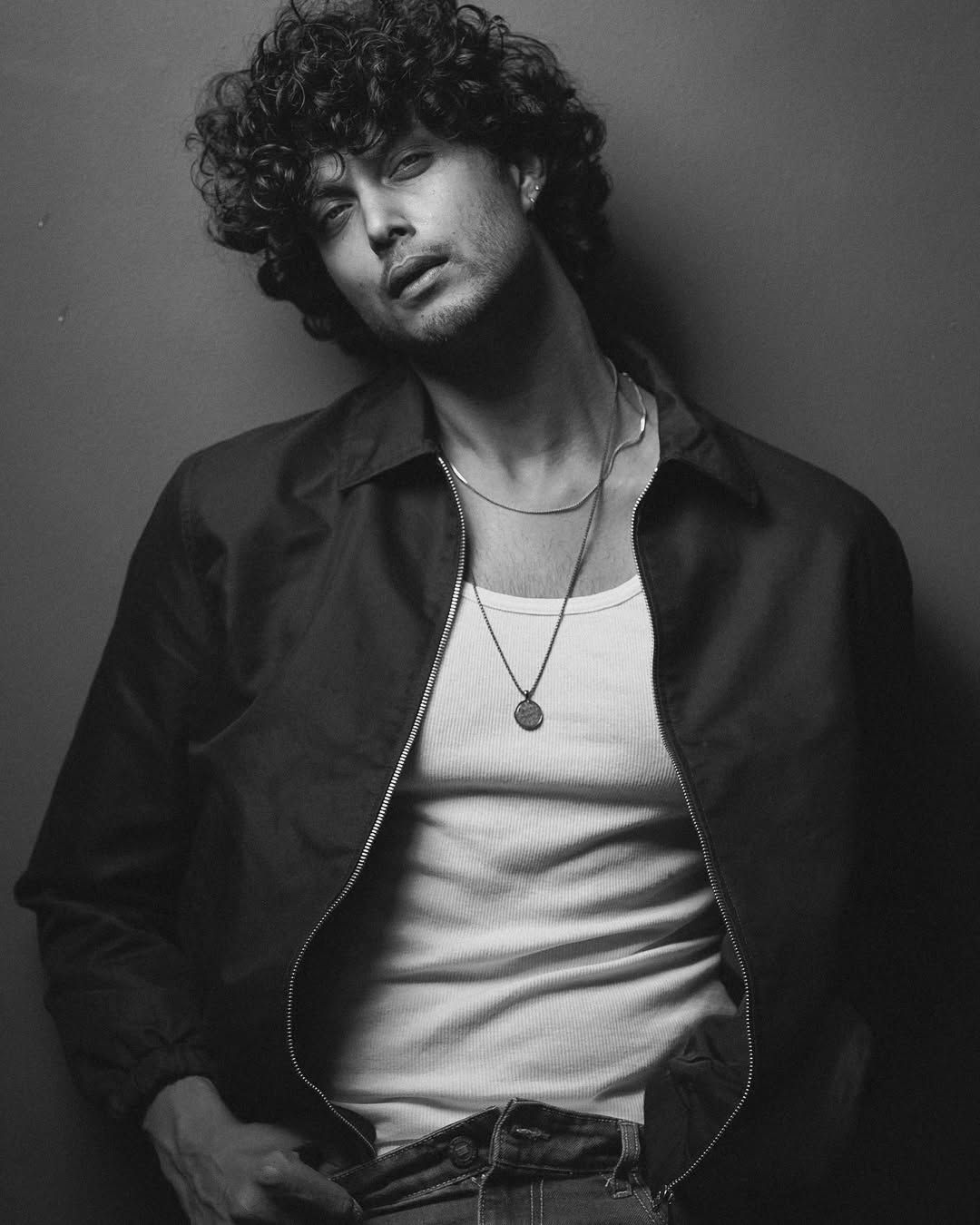 Creator Arjun Syam Gopan in a monochrome fashion portrait, wearing a casual layered outfit with curly hair and statement accessories