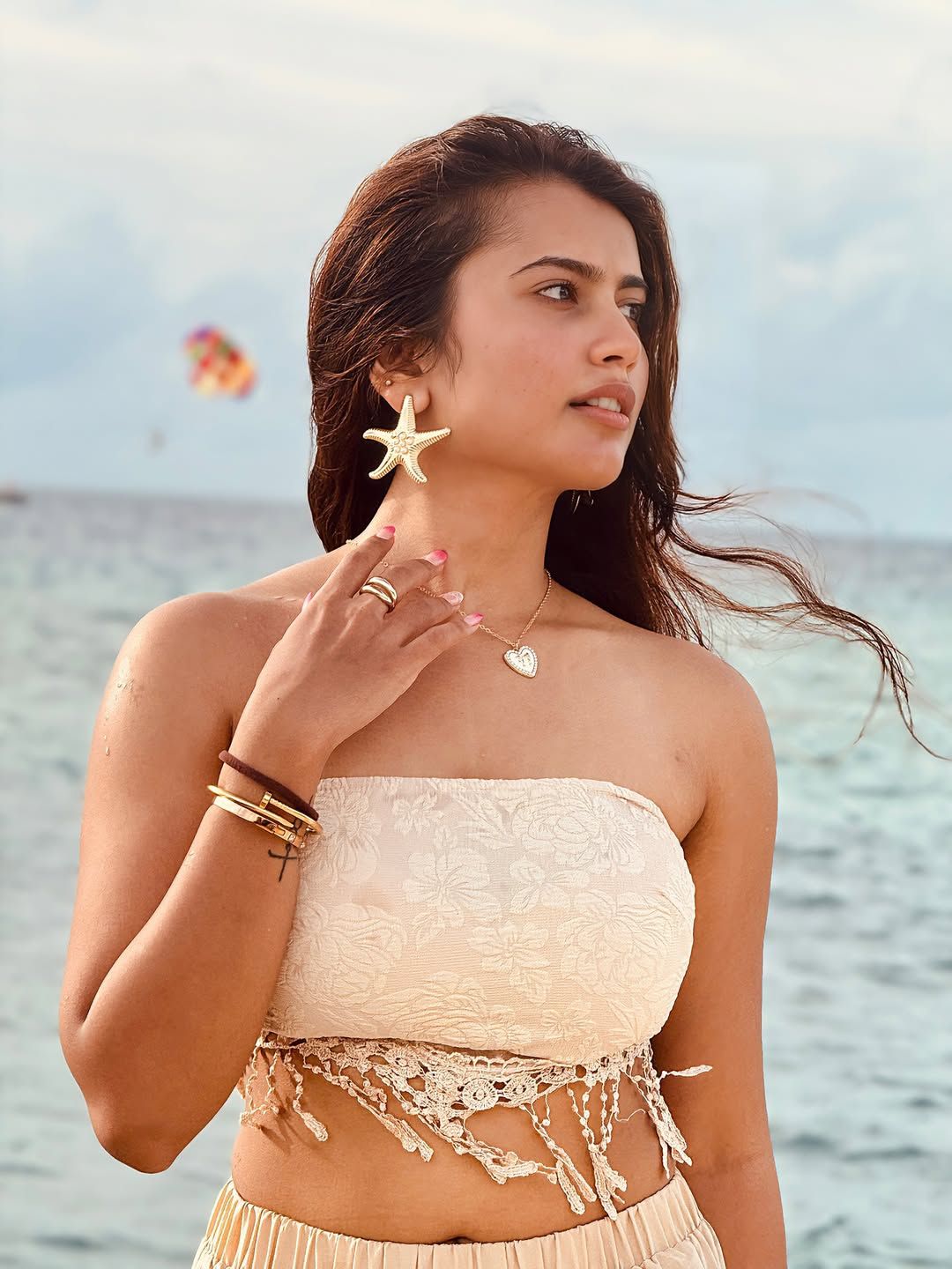 Creator Bunny Vox posing at the beach in a cream-colored summer outfit with ocean waves in the background