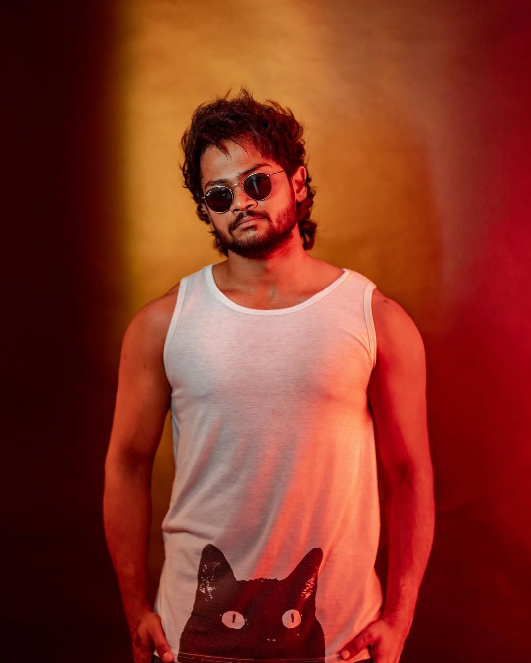 Creator Shanmukh Jaswanth wearing sunglasses and a casual sleeveless outfit, posing under dramatic red and orange studio lighting