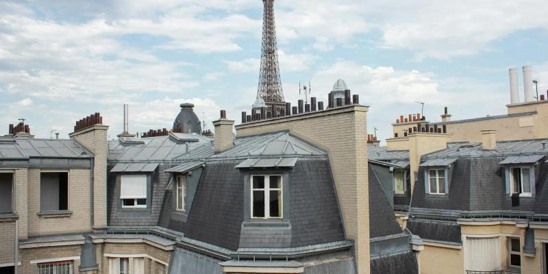 Zinc rooftops and dormer windows of Paris buildings, with the Eiffel Tower on the skyline