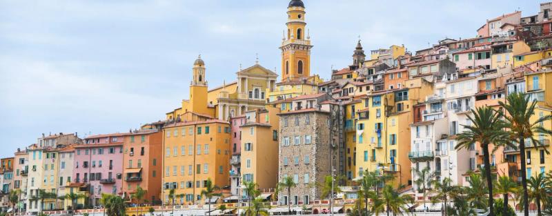 Colourful façades of Menton’s old town above the seafront and palm trees