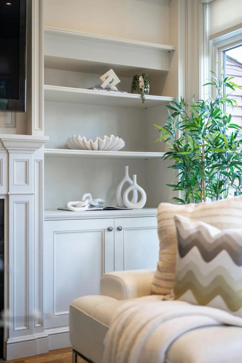 Renovated living room with built-in white shelving, a pale armchair and plants