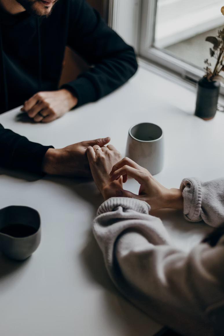 Two people at a table with coffee, hands gently touching