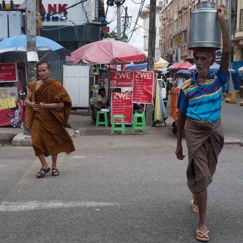 Some bloke crossing the street with a pail of milk on his head