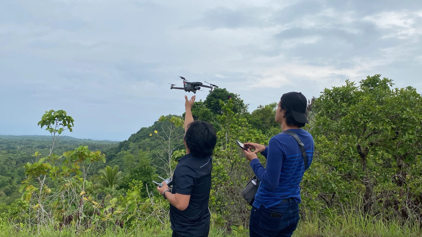 Two surveyors launching a drone from a ridge above forest canopy