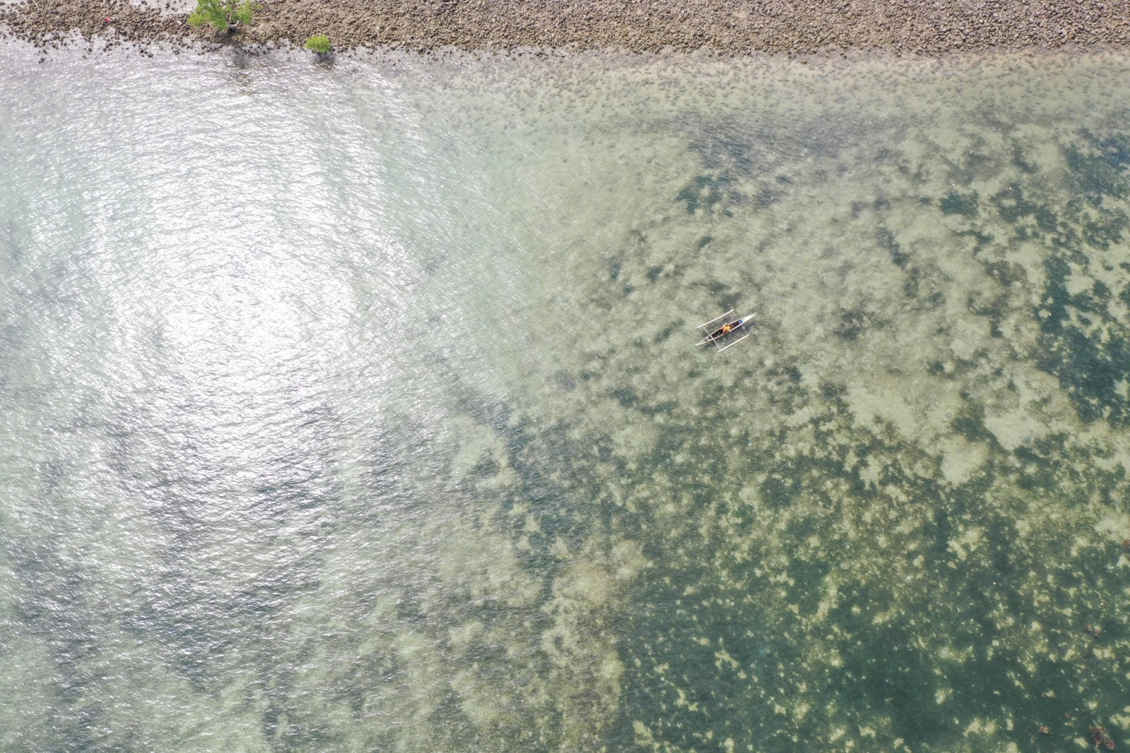 Aerial view of an outrigger boat on clear shallow water near a rocky shore