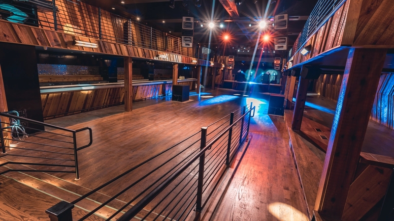 Wide Back of House shot of Ravine showcasing the wooden floors, black railing, balconies, production, and bars.