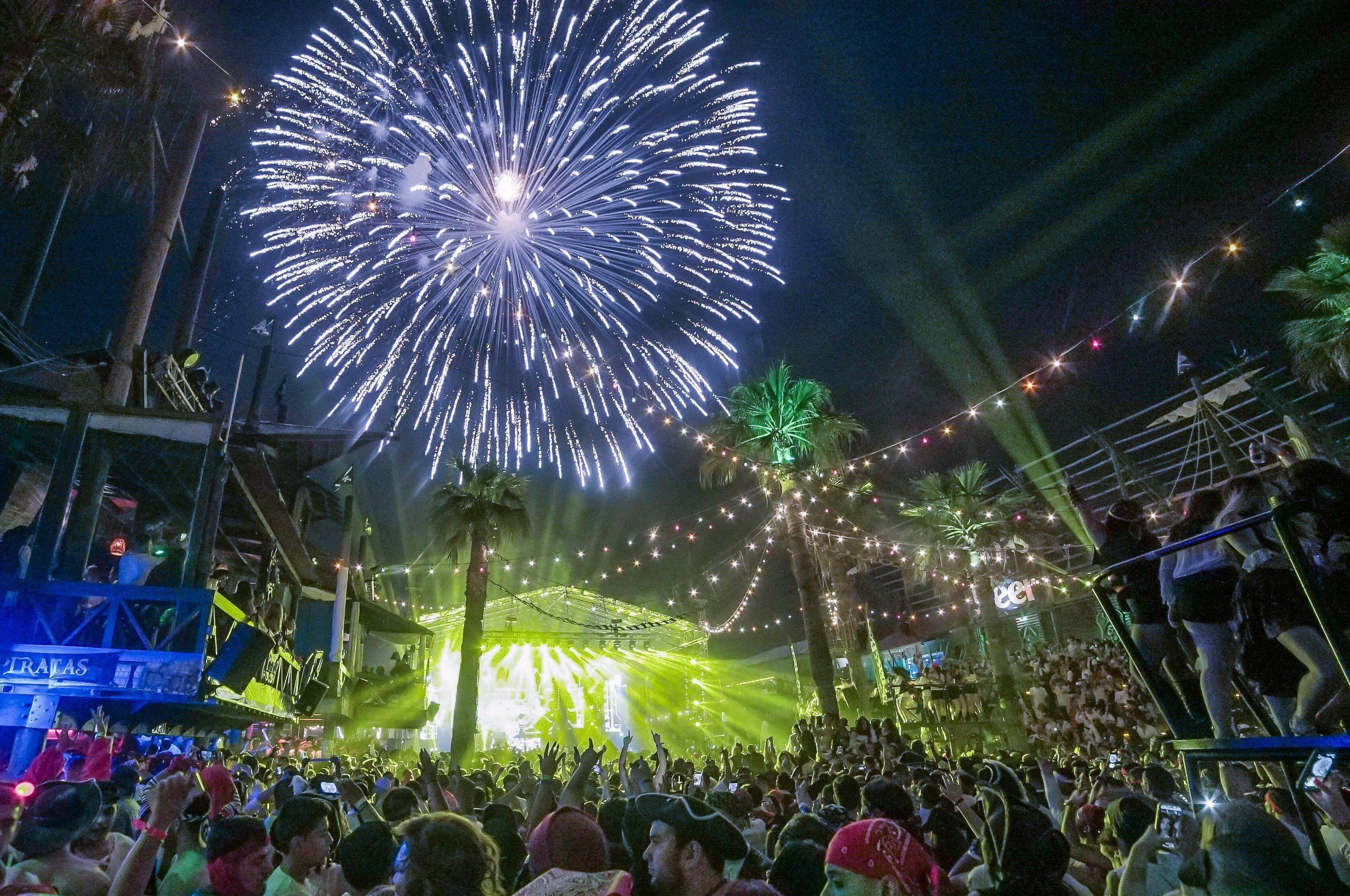 Fireworks illuminate the night sky over Papas & Beer at Rosarito, MX as a full crowd is illuminated by yellow producting lights from the stage