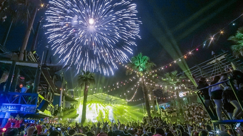 Fireworks illuminate the night sky over Papas & Beer at Rosarito, MX as a full crowd is illuminated by yellow producting lights from the stage