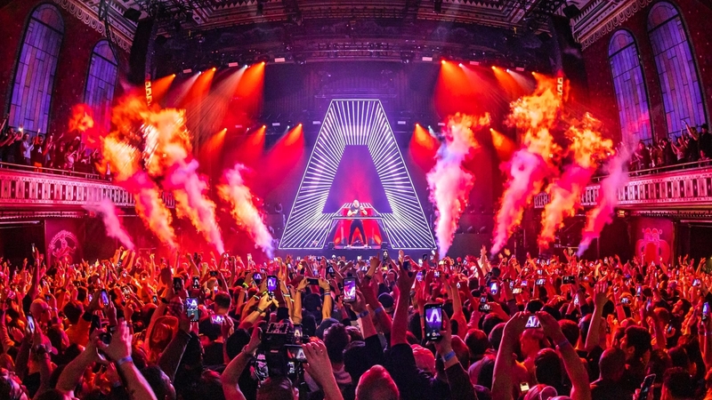 Crowd point of view shot of Armin Van Buuren performing in front of a packed crowd as CO2 bursts from either side of his "A" production DJ booth.