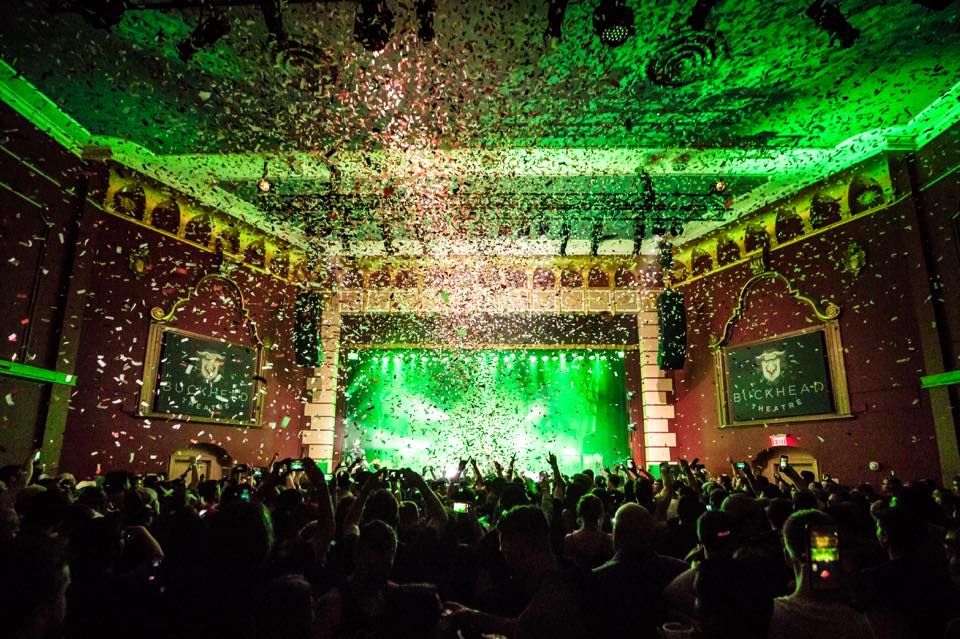 A crowd gathered in front of Buckhead Theatre main stage. Confetti is falling from the ceiling and is illuminated by the green production lights. 