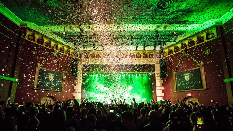 A crowd gathered in front of Buckhead Theatre main stage. Confetti is falling from the ceiling and is illuminated by the green production lights.