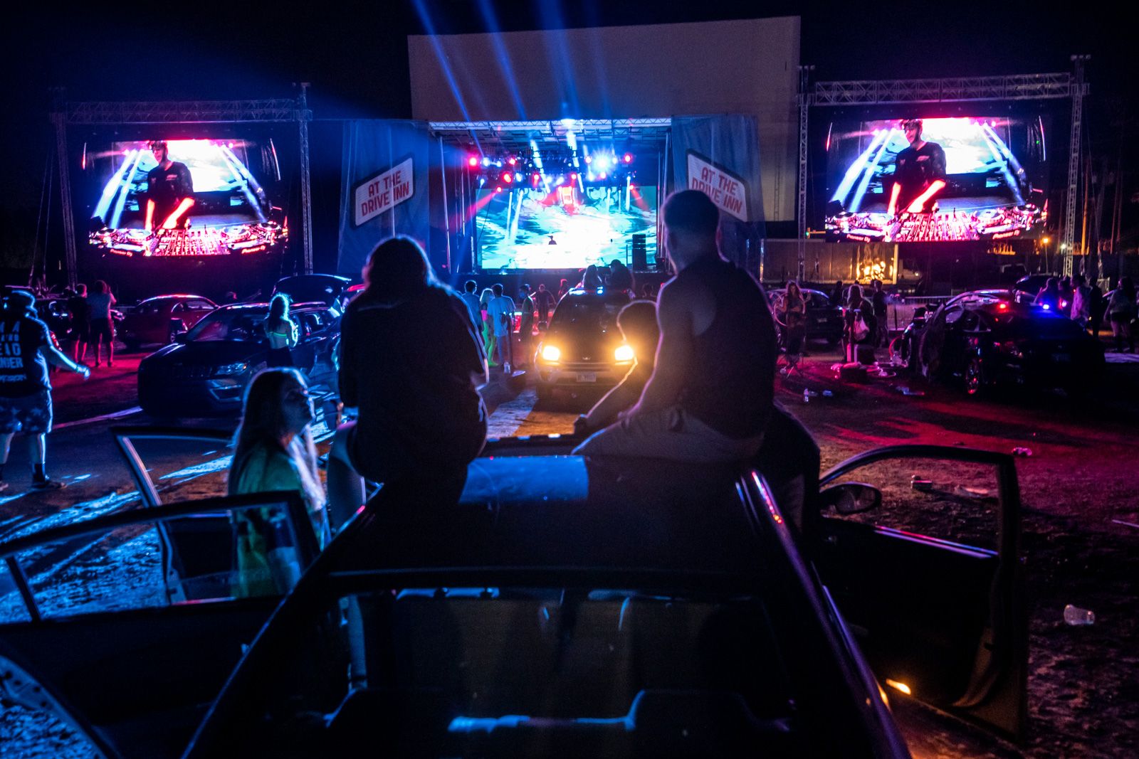 4 people in the center of the image on top of a car in front of the At The Drive Inn production at McHenry Outdoor Theater